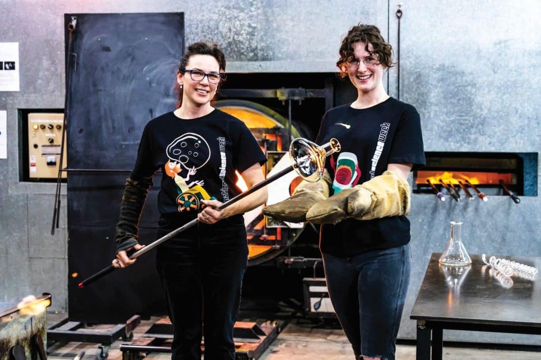 Two women blowing a glass beaker at the Canberra Glassworks hotshop