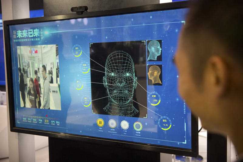 A man watches as a visitor tries out a facial recognition display