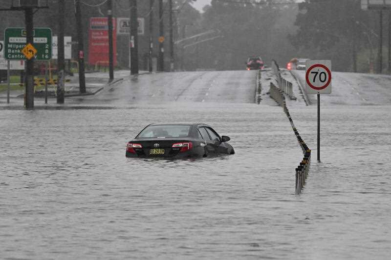 A car is seen abandoned in floodwaters on Newbridge Road in Chipping Norton in Western Sydney, Sunday, July 3, 2022