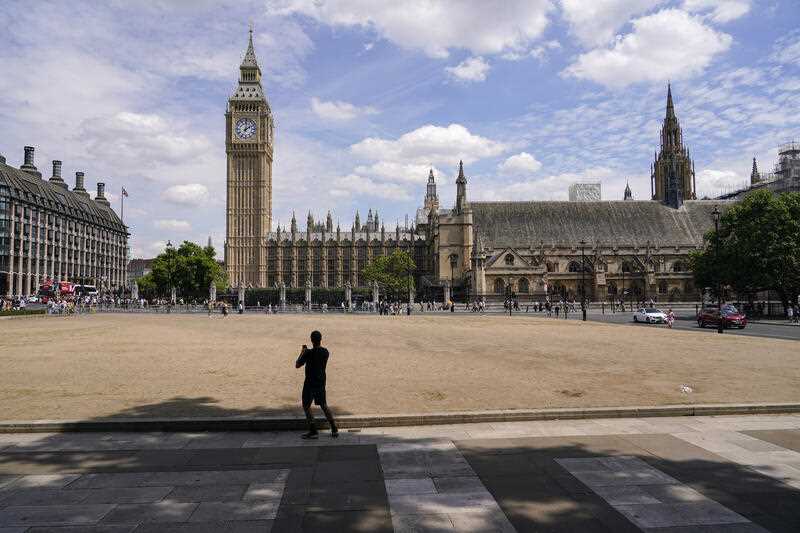 A man takes a picture in Parliament Square where the grass appears dry, in London, Wednesday, July 13, 2022