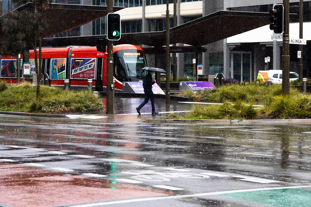 one lone pedestrian with an umbrella is seen near the light rail terminus in Canberra CBD