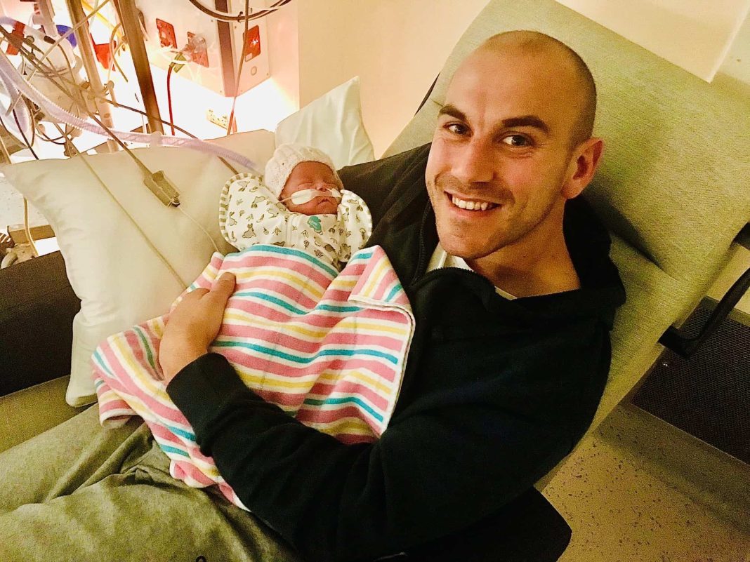 smiling dad holding tiny newborn daughter in Neonatal Intensive Care Unit