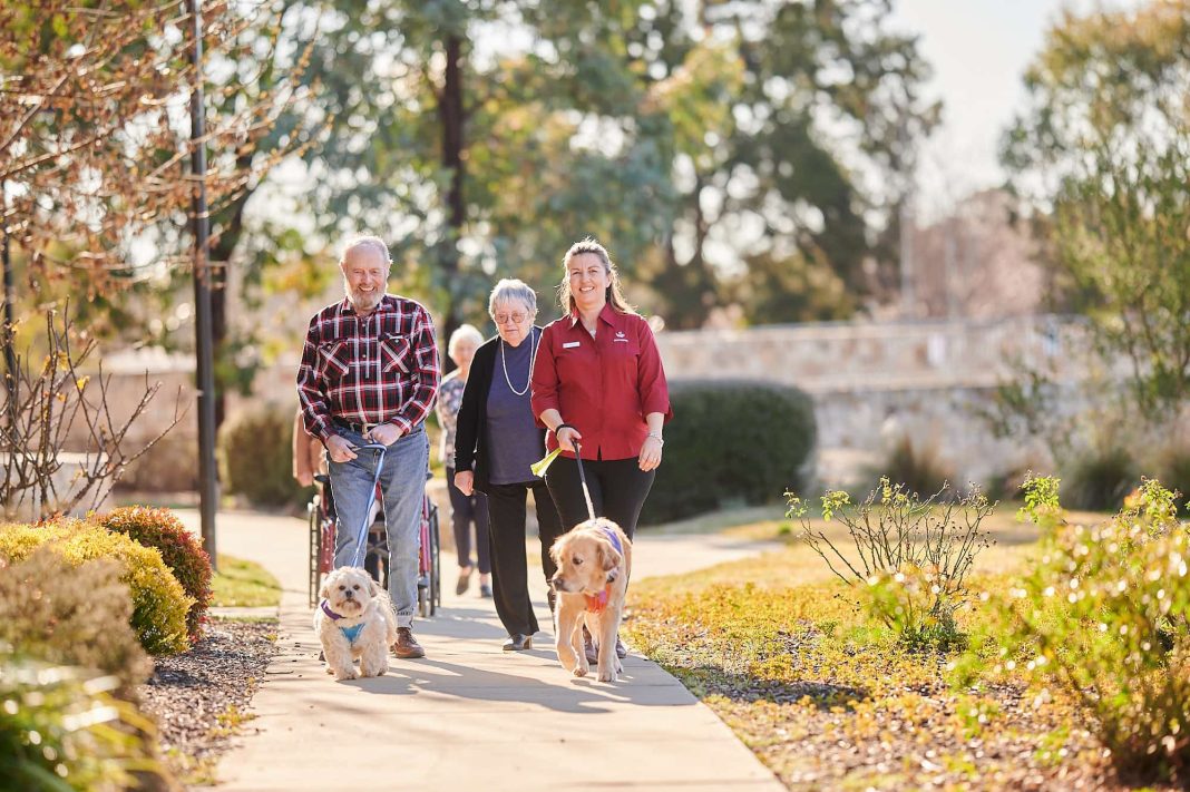 aged care worker with dog walking outdoors with a group of older residents