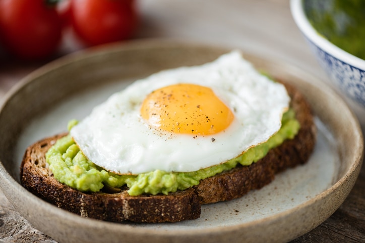 Toast with avocado and sunny side up egg on plate. Closeup view. Tasty breakfast or lunch food