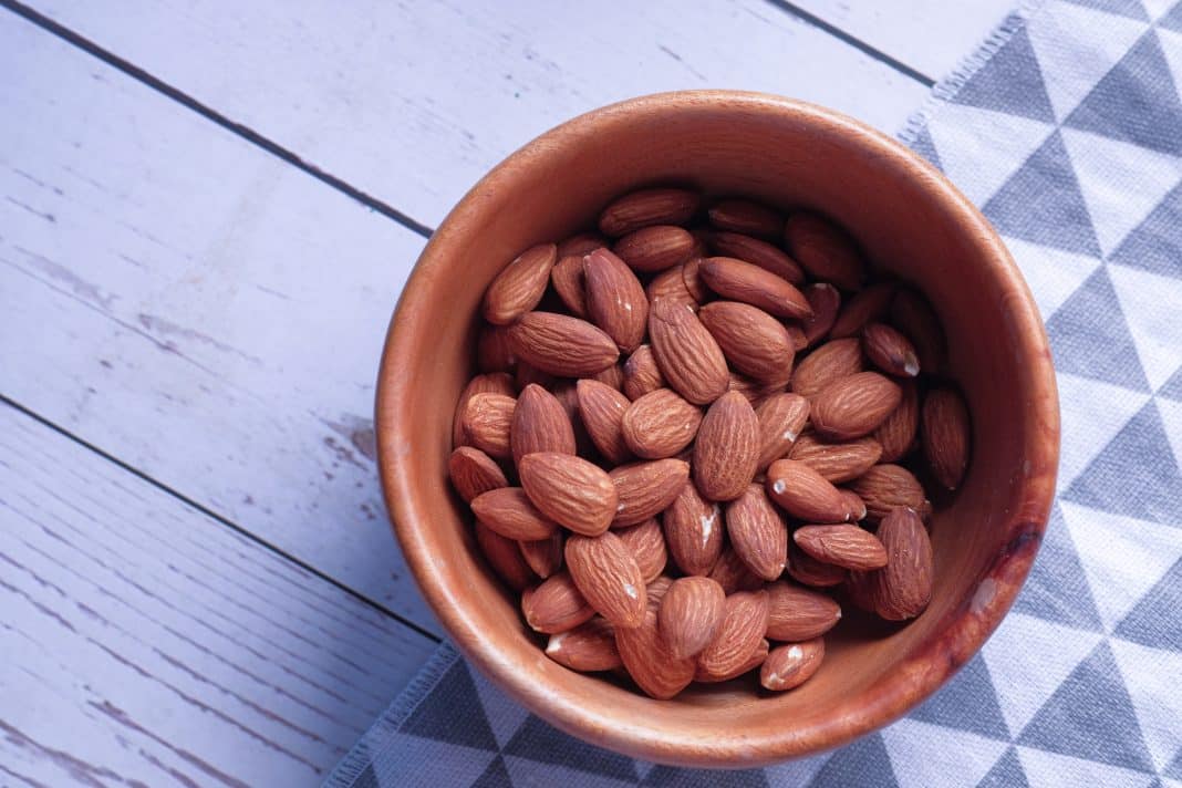 Bowl with tasty almonds on wooden table