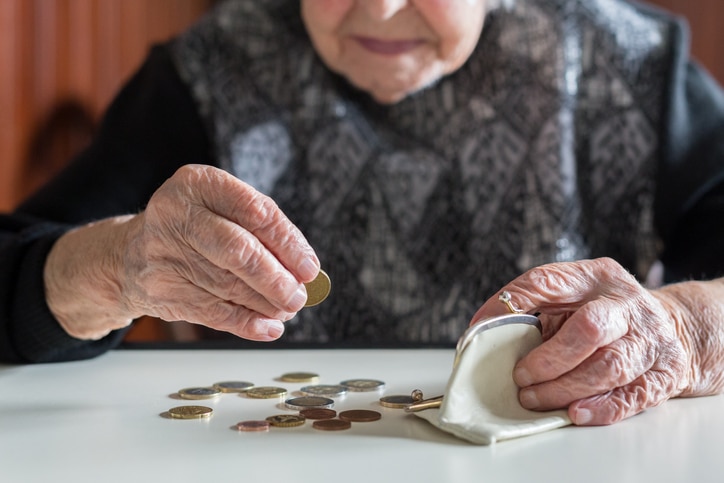Elderly woman sitting at the table at home and counting remaining coins from the pension in her wallet after paying the bills.