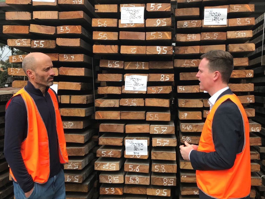two men standing in front of stacks of salvaged timber
